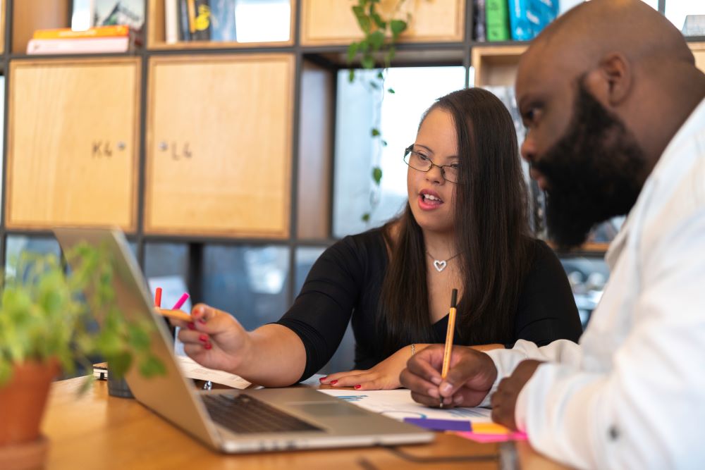 Image shows two people sitting in front of a laptop studying