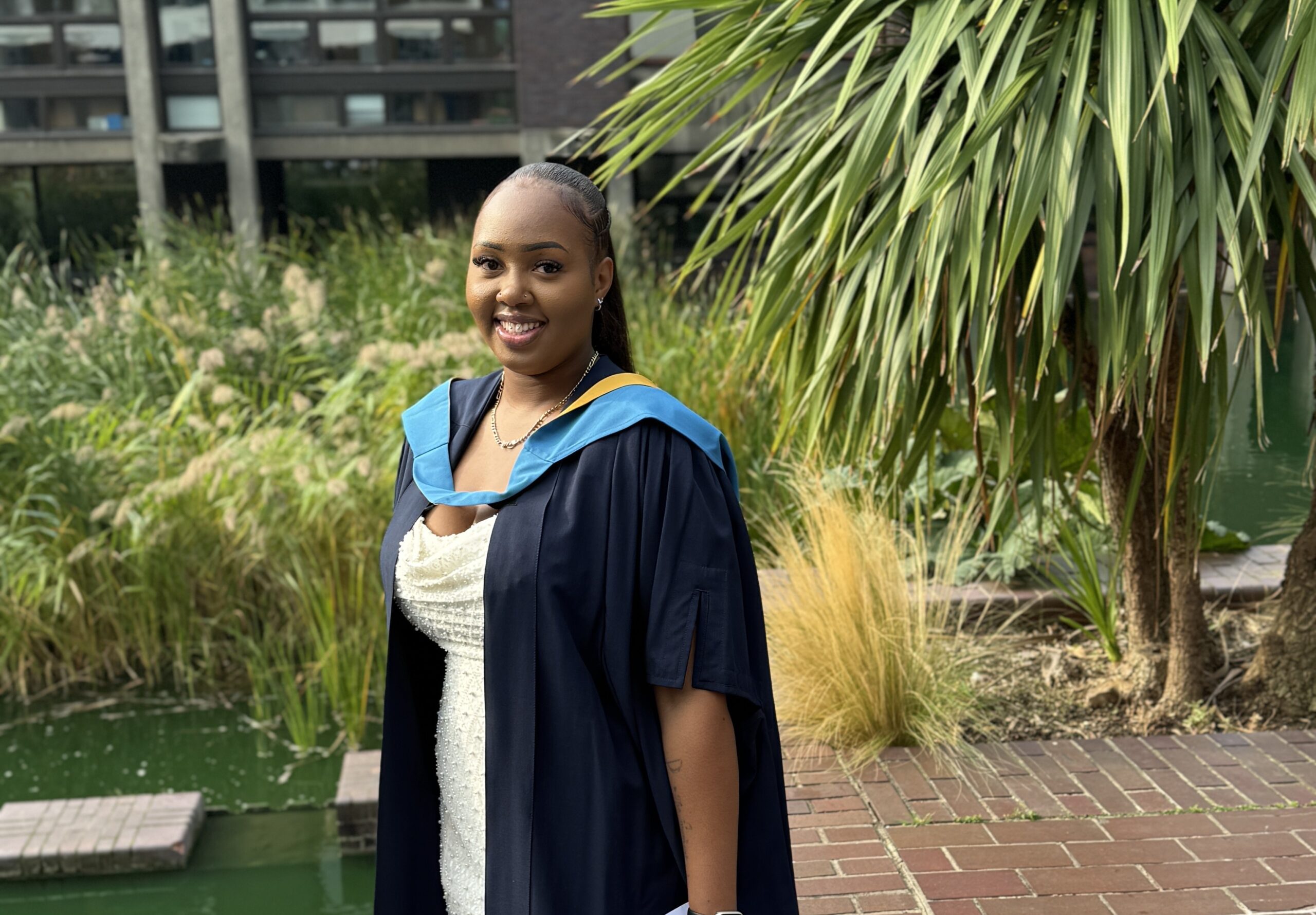 Leonie dressed in graduation gown, smiling at the camera with a tree in the background.